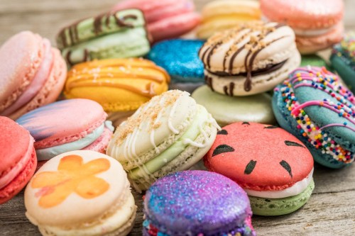 A colorful assortment of macarons in various flavors and designs, arranged on a wooden surface.