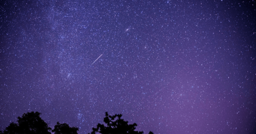 A starry night sky filled with twinkling stars and a faint meteor streaking across a purple-hued background.