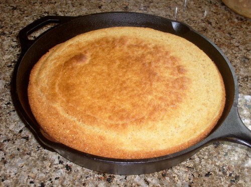 A golden-brown cornbread baked in a cast iron skillet on a granite countertop.