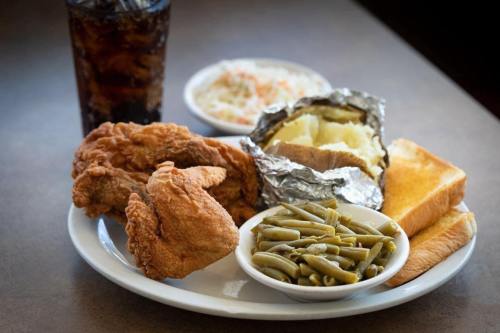 A plate of fried chicken, green beans, baked potato, coleslaw, toast, and a glass of cola.