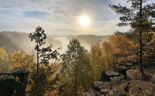 A misty landscape at sunrise, featuring autumn trees and rocky outcrops under a soft, golden light.