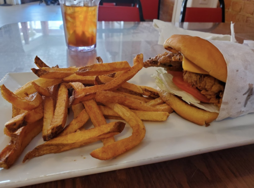 A plate with a fried chicken sandwich and a side of golden French fries, accompanied by a glass of iced tea.