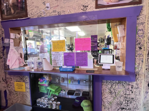 A colorful counter with signs, tips jar, and various items in a graffiti-decorated shop interior.