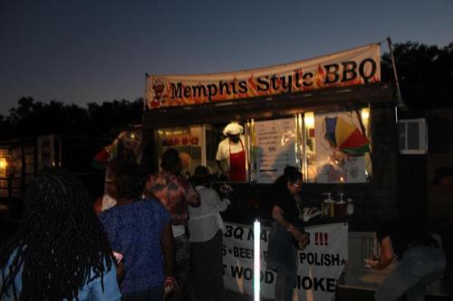 A food truck with a "Memphis Style BBQ" sign, serving customers in a dimly lit outdoor setting.