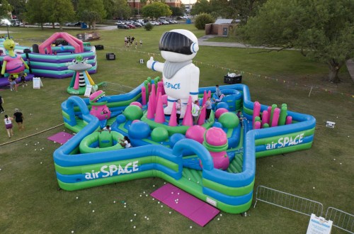 A colorful inflatable play area with an astronaut figure, featuring slides and obstacles in a park setting.