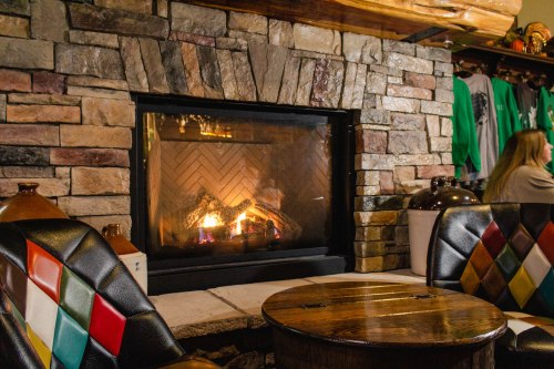 Cozy fireplace with a stone surround, wooden table, and colorful chairs in a warm, inviting setting.