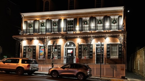 A beautifully lit historic building at night, featuring festive decorations and a gift shop sign.