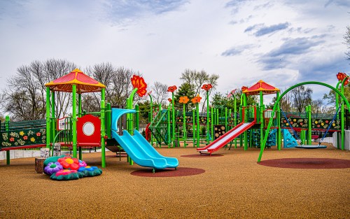 Colorful playground with slides, climbing structures, and flower decorations under a cloudy sky.