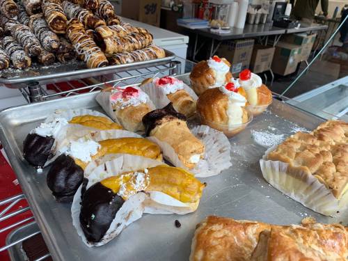 A tray of assorted pastries, including cream-filled rolls, fruit-topped desserts, and chocolate-dipped treats.