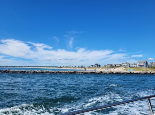 A scenic view of a coastline with houses, blue sky, and gentle waves from a boat.