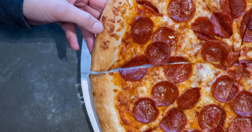 A hand reaching for a slice of pepperoni pizza on a dark table.