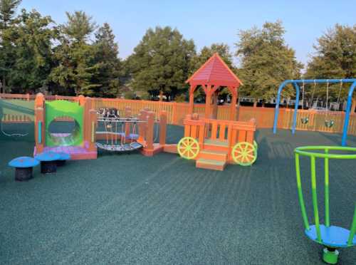 Colorful playground equipment with a playhouse, swings, and climbing structures on a green rubber surface.