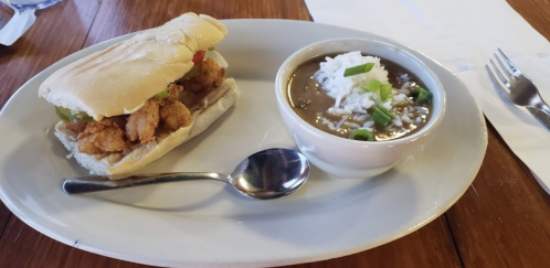 A plate with a shrimp sandwich and a bowl of black-eyed peas topped with green onions and rice.