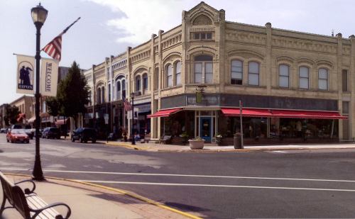 Historic buildings line a charming street, featuring shops and a welcoming banner in a small town.
