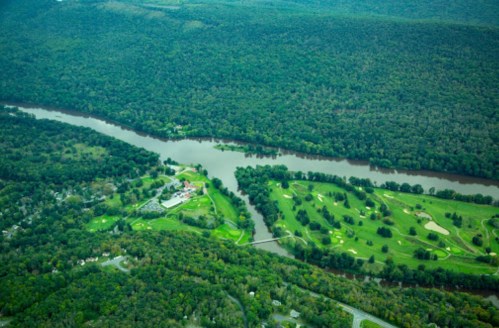 Aerial view of a lush green landscape with a river, golf course, and wooded areas.