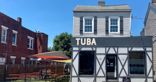 A small, two-story building with "TUBA" sign, featuring outdoor seating and a clear blue sky.