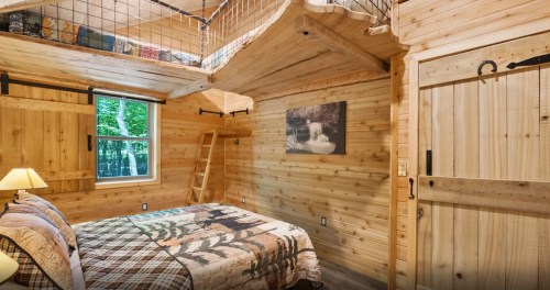 Cozy wooden cabin interior featuring a bed, lofted sleeping area, and rustic decor.