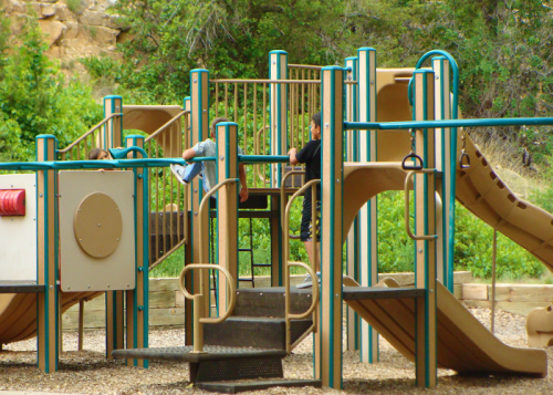 Children playing on a colorful playground with slides and climbing structures, surrounded by greenery.
