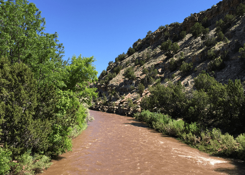 A winding river flows through a rocky landscape, flanked by green trees under a clear blue sky.