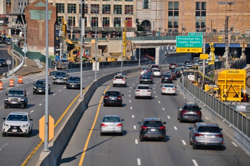 Traffic flows on a busy highway with construction in the background and an exit sign for Copley Square.