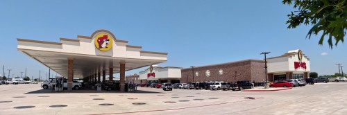 A wide view of a busy gas station and convenience store with a large sign featuring a cartoon dog.