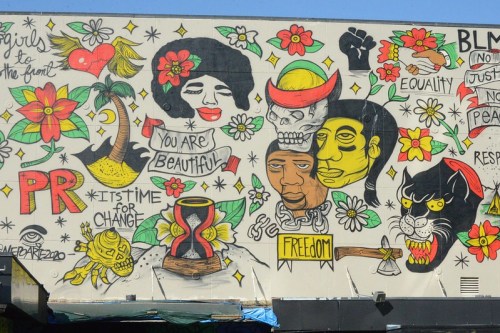Colorful mural featuring diverse faces, messages of beauty, freedom, equality, and social change.