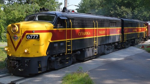 A vintage yellow and black train with "Cuyahoga Valley" markings, parked on a track surrounded by greenery.