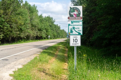 Sign for the Lady Slipper Scenic Byway, indicating a natural preservation route along a tree-lined road.