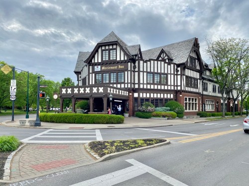 A Tudor-style building with a sign reading "Mansion Inn," surrounded by greenery and a cloudy sky.
