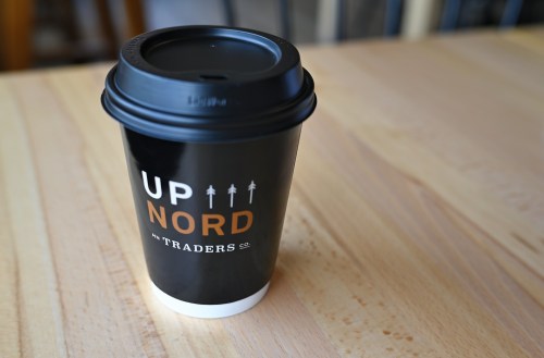 A black coffee cup with the text "UP NORD TRADERS CO" on a wooden table.