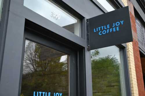 Sign for "Little Joy Coffee" on a storefront, with a modern design and large windows.