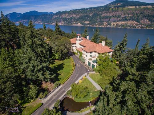 Aerial view of a large house surrounded by trees, near a river with mountains in the background.