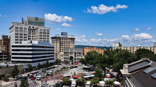 A vibrant cityscape featuring buildings, a busy street, and a clear blue sky with fluffy clouds.