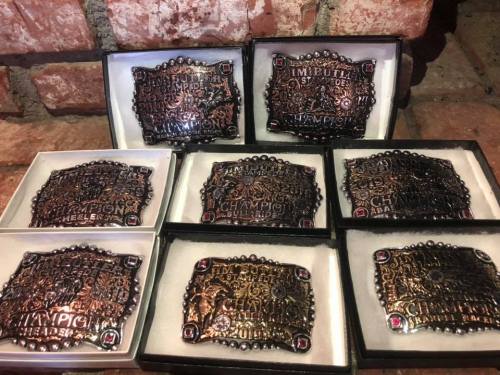 A collection of ornate championship belt buckles displayed in black boxes, featuring intricate designs and gemstones.