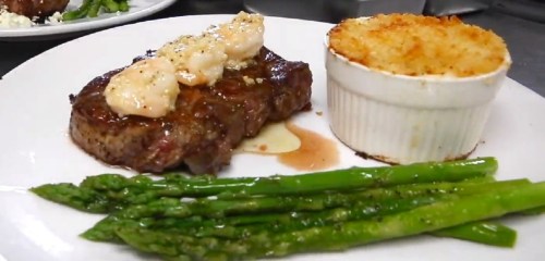 A plate featuring a grilled steak with butter, asparagus, and a ramekin of cheesy potato gratin.