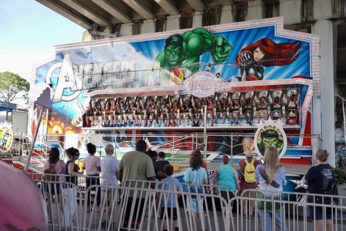 A colorful amusement ride themed after the Avengers, with riders seated and a crowd watching below.