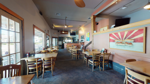 Interior of a casual restaurant featuring wooden tables, chairs, and a colorful sandwich mural on the wall.