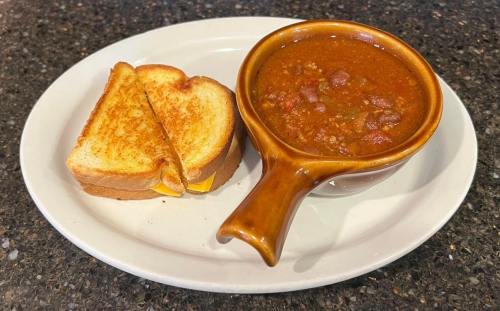 A bowl of chili with beans served alongside a grilled cheese sandwich on a white plate.
