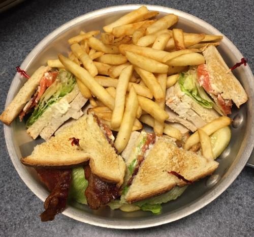 A metal plate with a club sandwich and a generous serving of French fries.