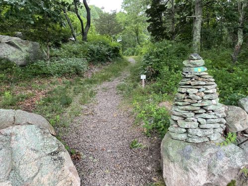 A gravel path leads through a lush green area, marked by a stacked stone cairn on the right.