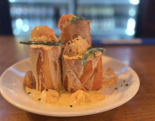 A plate of shrimp-stuffed bread rolls topped with creamy sauce and garnished with green herbs.