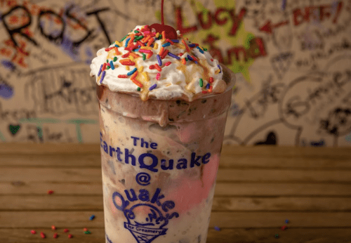 A colorful ice cream sundae topped with whipped cream, sprinkles, and a cherry in a clear cup.
