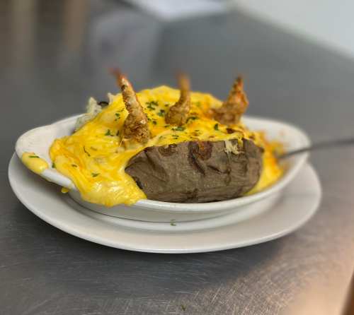 A baked potato topped with melted cheese and garnished with crispy shrimp, served in a white dish on a plate.