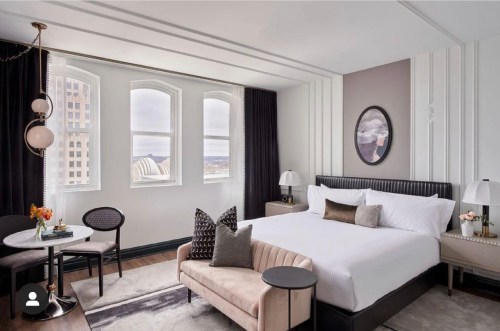 Modern hotel room featuring a king bed, stylish decor, large windows, and a cozy seating area.