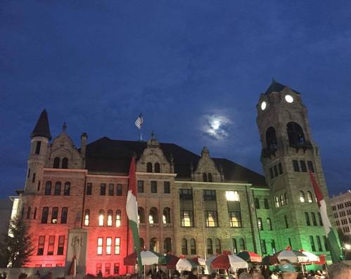 Historic building illuminated in red and green lights at night, with a cloudy sky and a visible moon.
