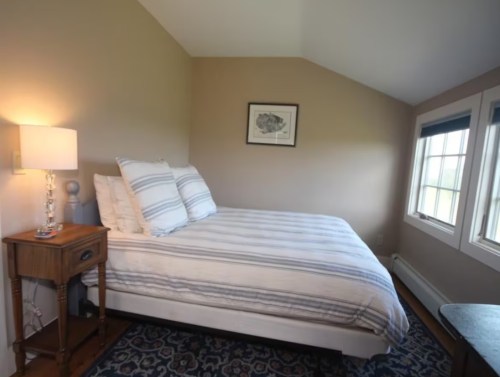 Cozy bedroom with a striped bed, bedside table, and large windows letting in natural light.