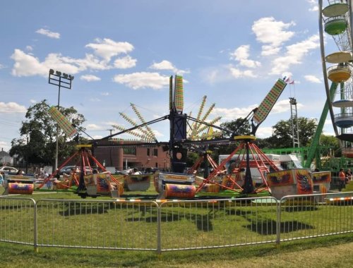A colorful amusement park ride with spinning arms, surrounded by a grassy area and a Ferris wheel in the background.
