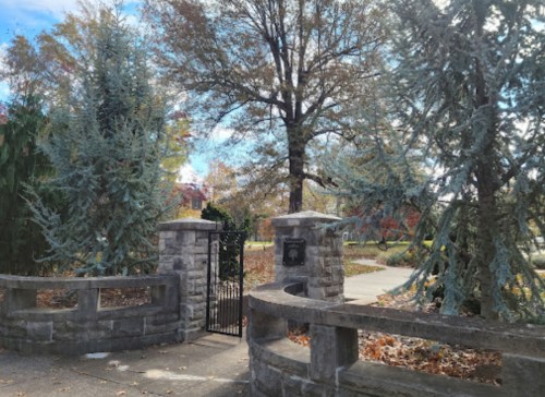 A stone gate surrounded by trees, with colorful autumn foliage in the background.