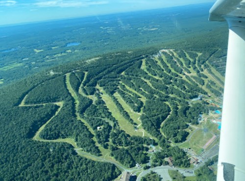 Aerial view of a lush, green hillside with winding paths and a water park at the base, under a clear blue sky.