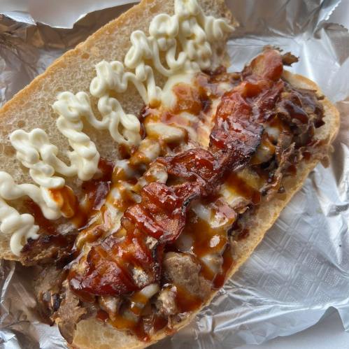 A sandwich with meat, crispy bacon, barbecue sauce, and mayonnaise on a toasted bun, wrapped in foil.
